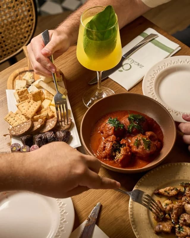 Mesa con un guiso de albóndigas, tapas para compartir y un cóctel